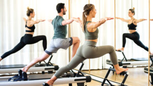 A class in a gym doing pilates standing lunges in front of a mirror