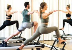 A class in a gym doing pilates standing lunges in front of a mirror